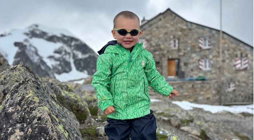 Little boy in namuk clothing running toward the camera, smiling, with the Tierbergli hut in the background