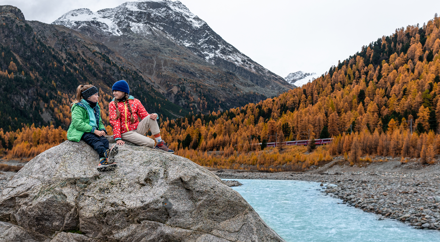Two kids sitting on a rock in the middle of the nature of Engadin