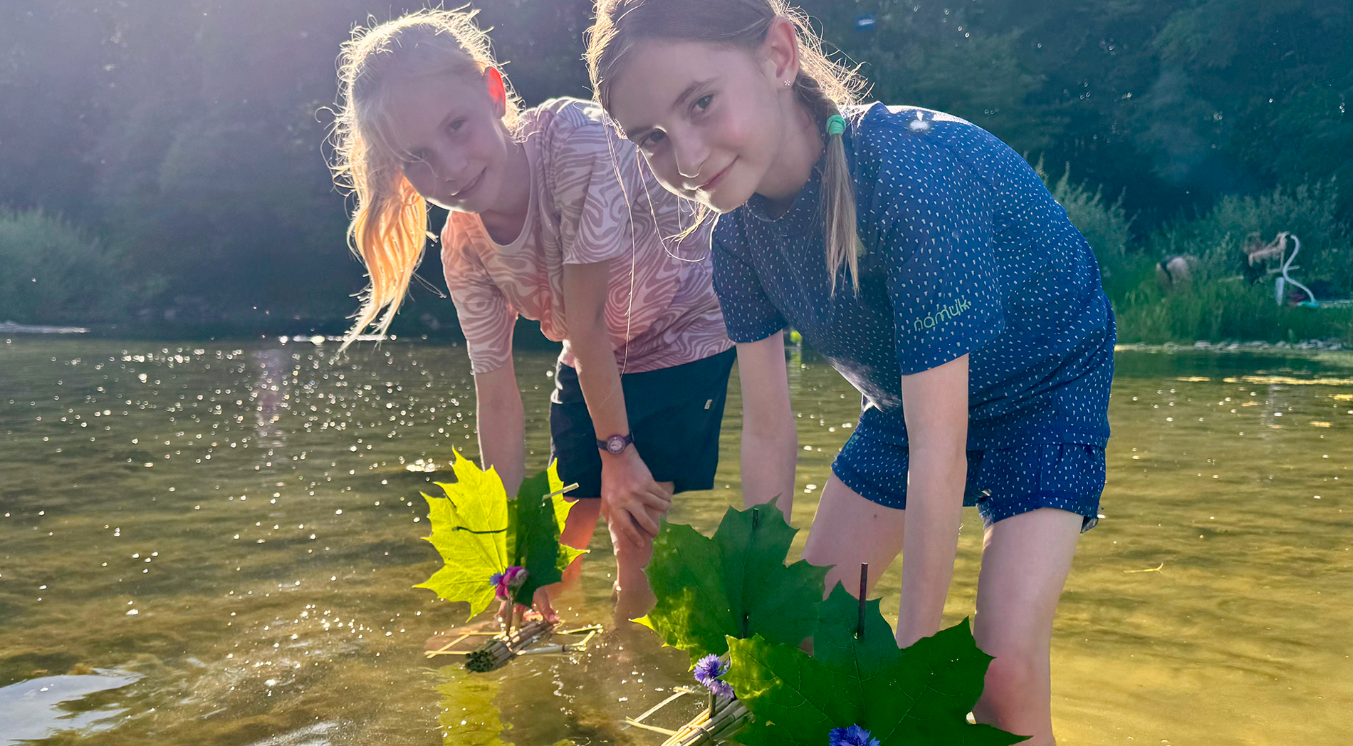 Two girls are standing in the water with their decorated reed boats