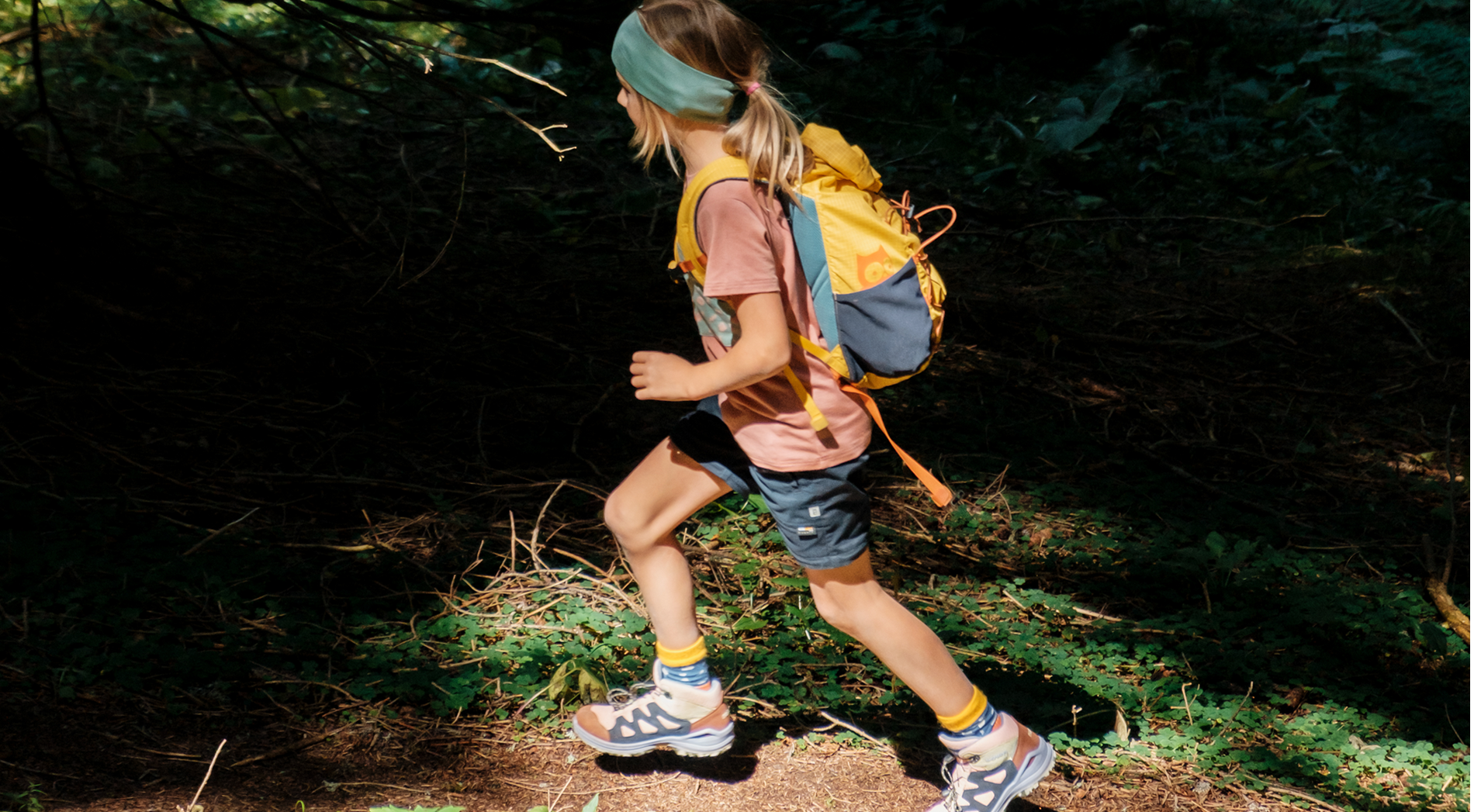Hiking with children: girl hiking through the forest wearing namuk clothing and carrying a namuk backpack
